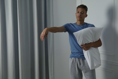 Photo of Young man with pillow suffering from sleepwalking at home, space for text