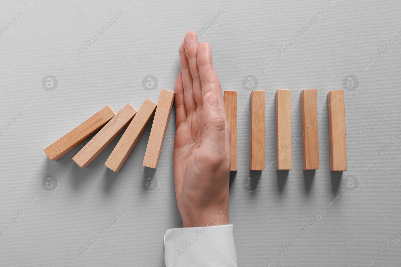 Photo of Man stopping wooden blocks from falling on grey background, top view. Domino effect