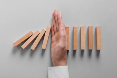 Photo of Man stopping wooden blocks from falling on grey background, top view. Domino effect