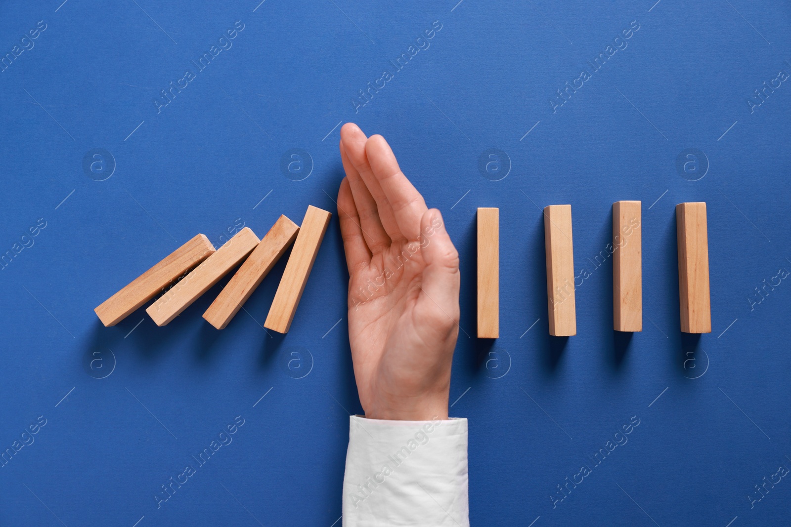 Photo of Man stopping wooden blocks from falling on blue background, top view. Domino effect