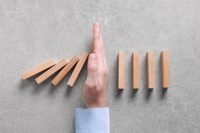 Photo of Man stopping wooden blocks from falling on grey background, top view. Domino effect