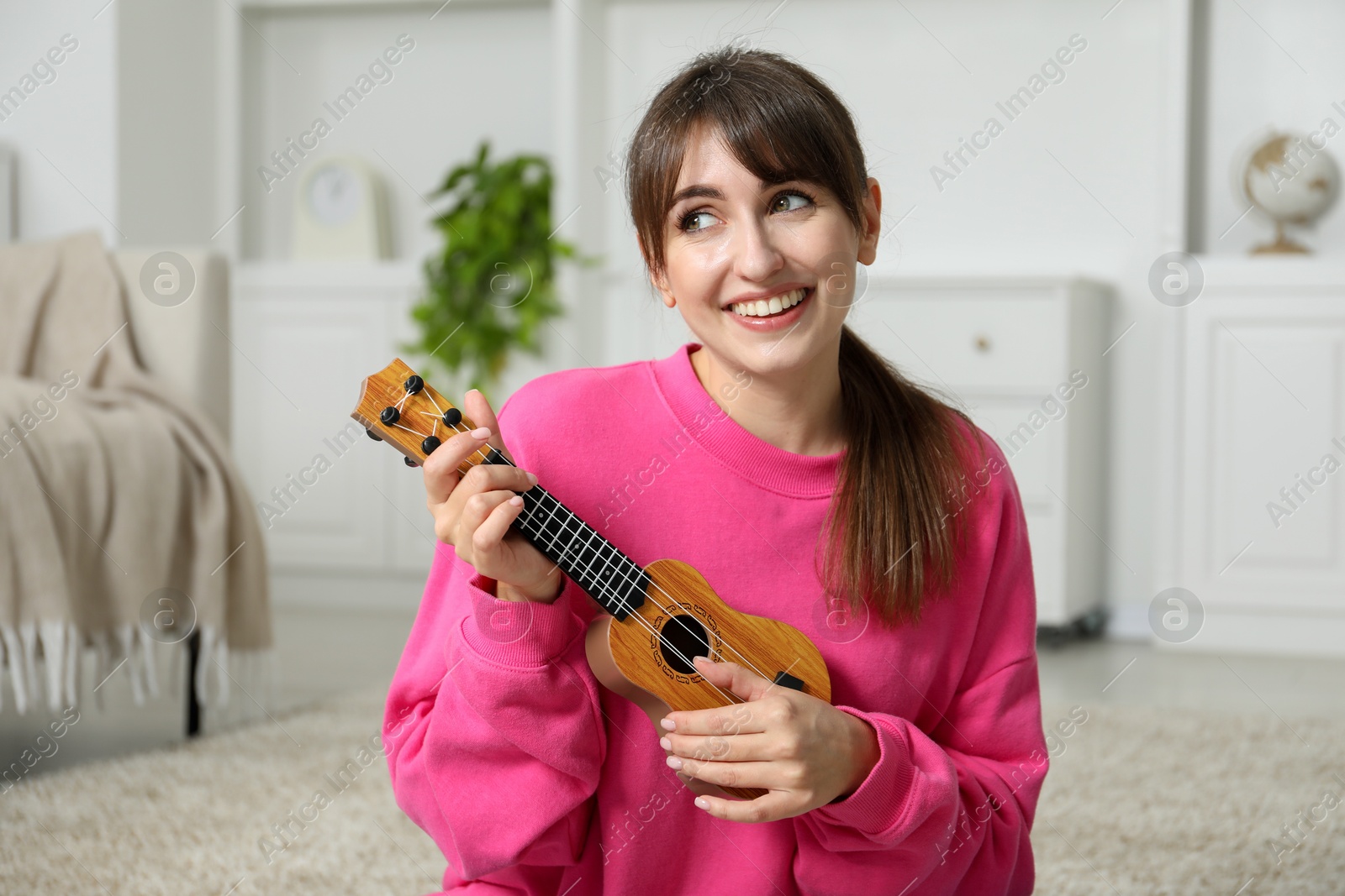 Photo of Happy woman playing ukulele on floor at home