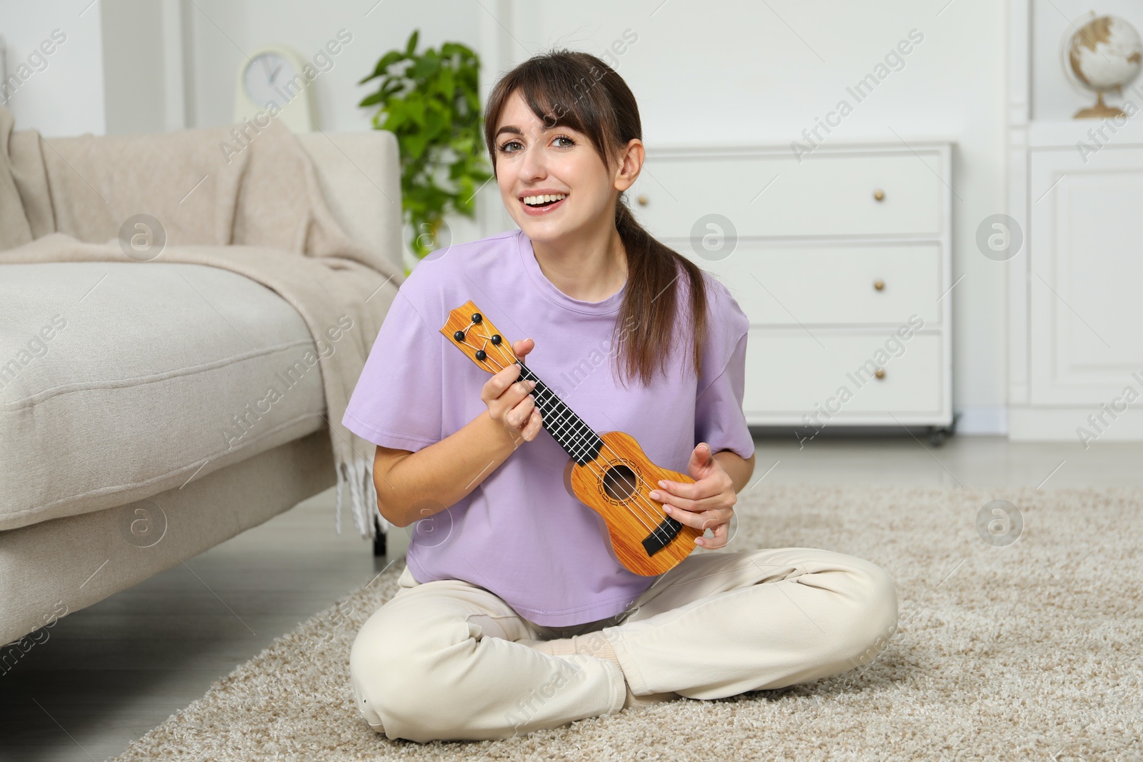 Photo of Happy woman playing ukulele on floor at home