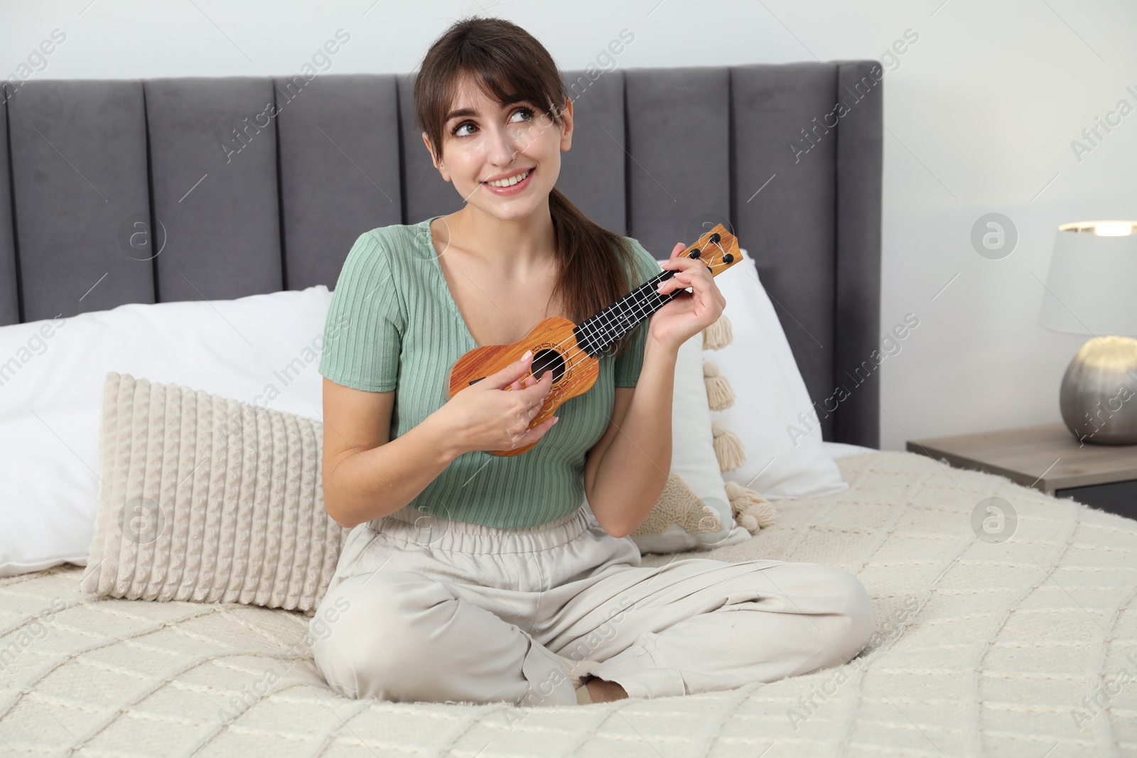 Photo of Happy woman playing ukulele on bed at home