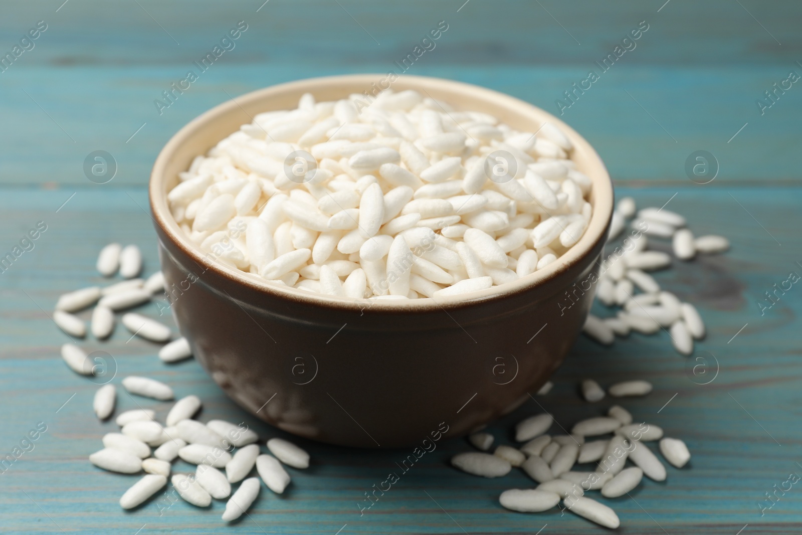 Photo of Puffed rice in bowl on light blue wooden table, closeup