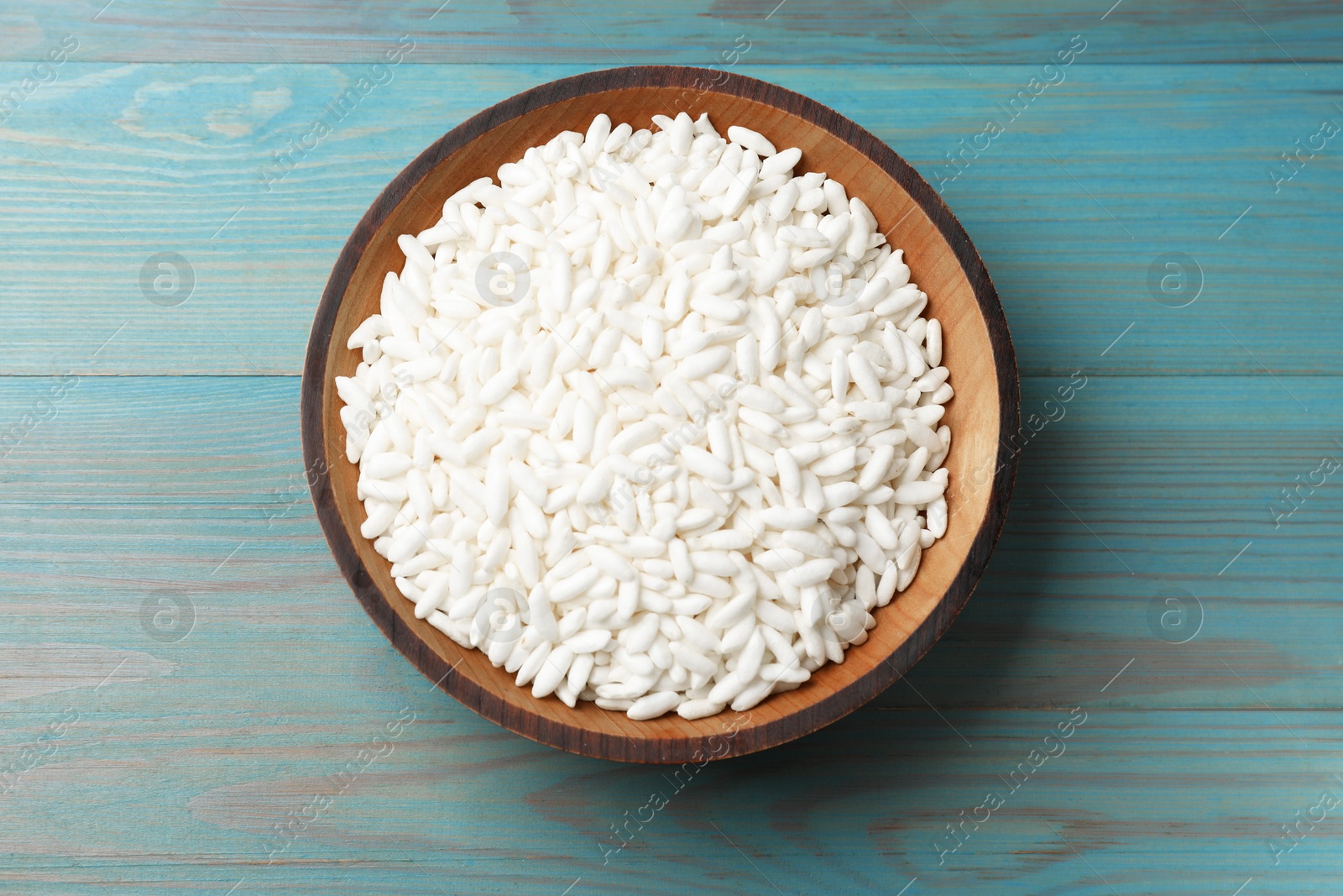 Photo of Puffed rice in bowl on light blue wooden table, top view