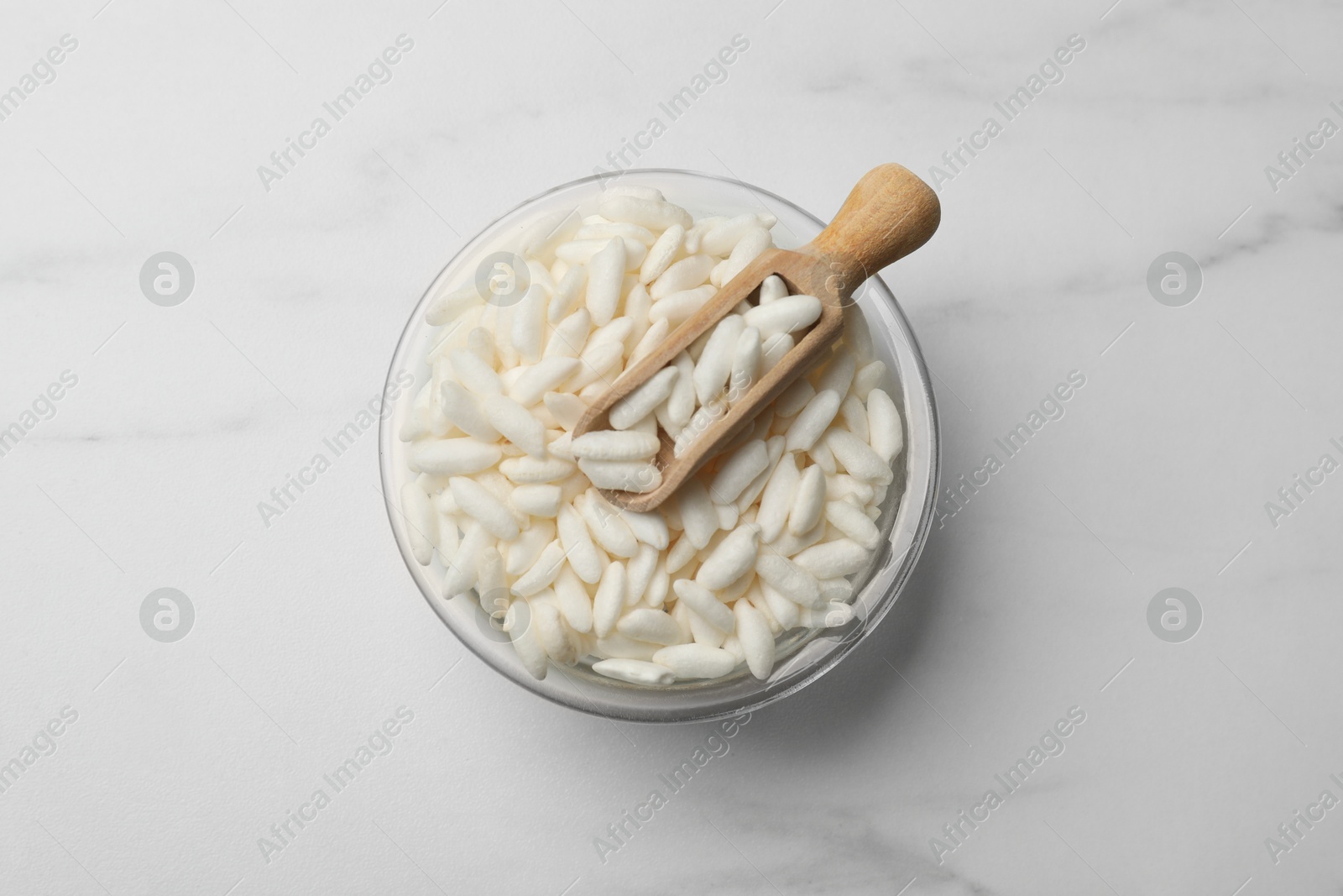 Photo of Puffed rice in bowl and scoop on white marble table, top view