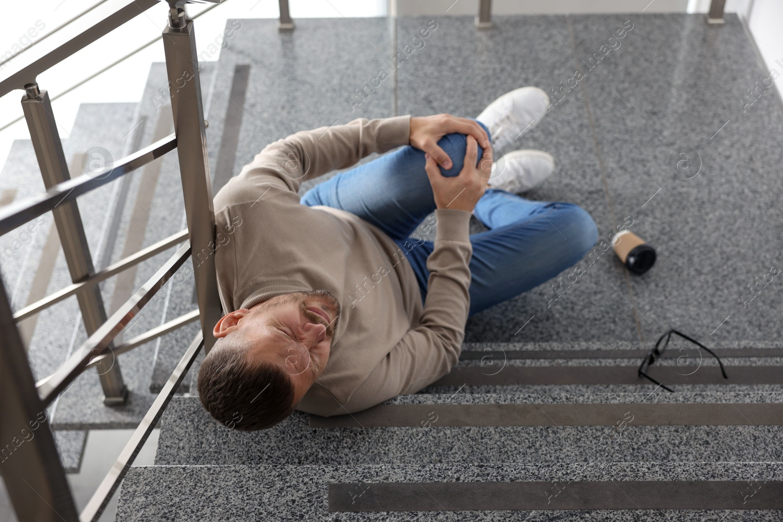 Photo of Man with injured knee on stairs in building after fall, above view. Dangerous accident