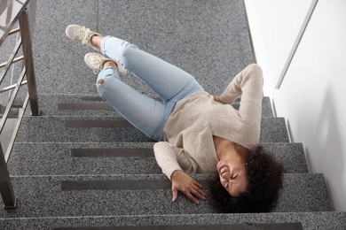 Injured woman on stairs in building after fall, above view. Dangerous accident