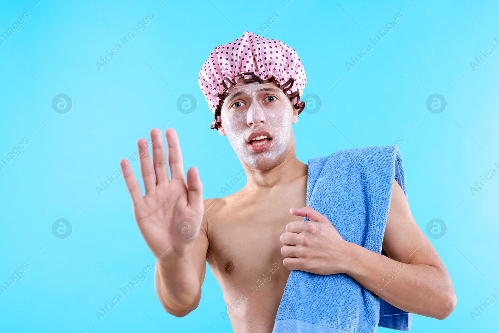 Photo of Man with shower cap and towel making stop gesture on light blue background