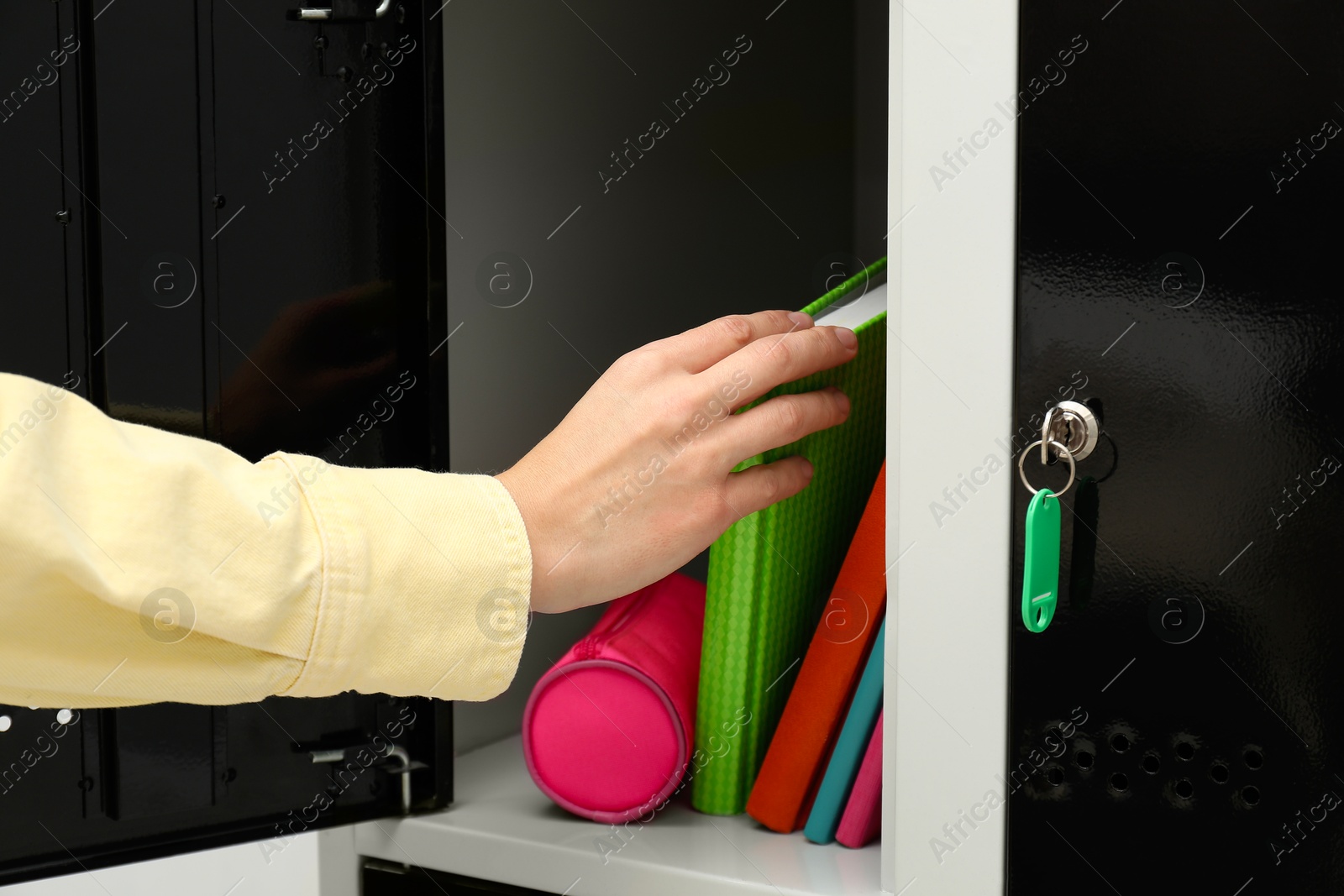 Photo of Woman putting book into locker indoors, closeup