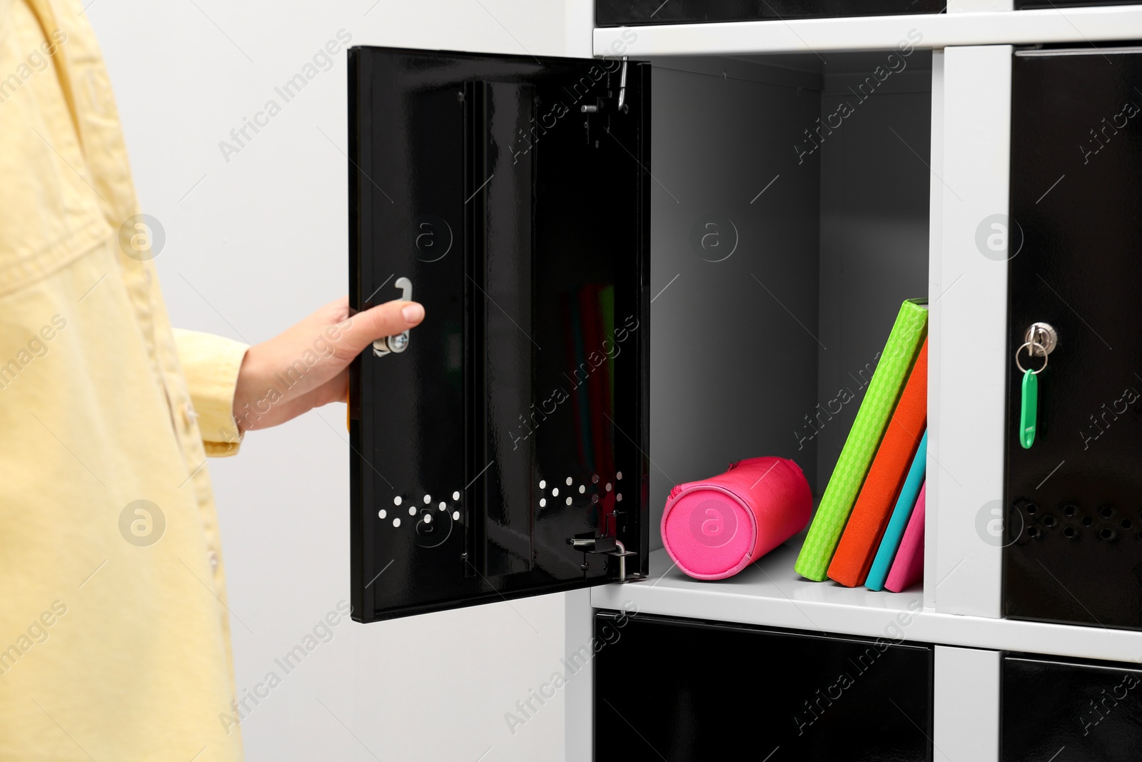 Photo of Woman closing personal locker with school supplies indoors, closeup