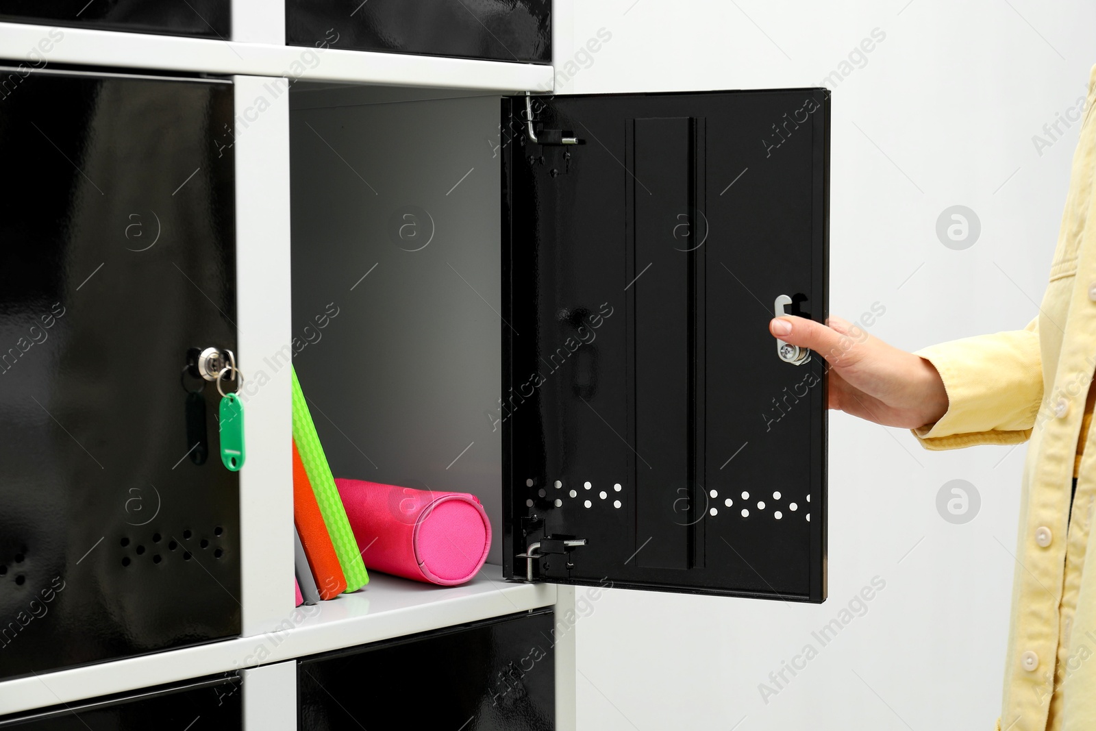 Photo of Woman closing personal locker with school supplies indoors, closeup