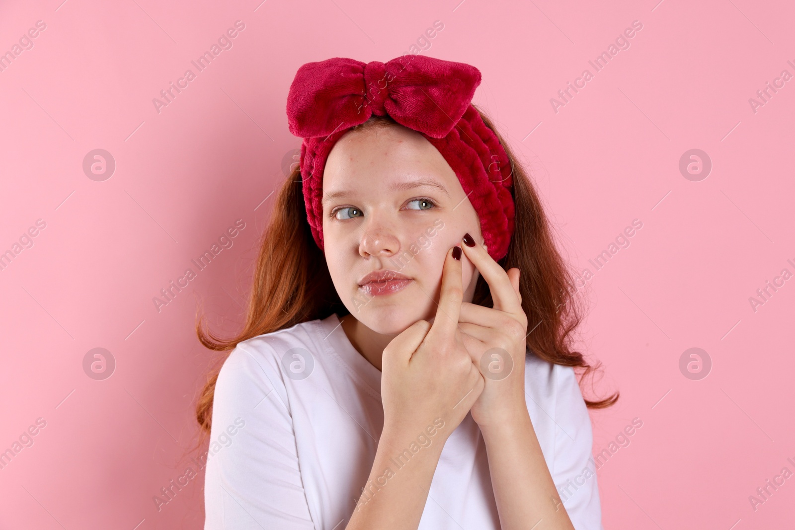 Photo of Teenage girl popping pimple on her face against pink background. Acne problem