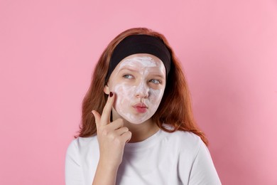 Photo of Teenage girl applying mask on her face with against pink background. Cosmetic product