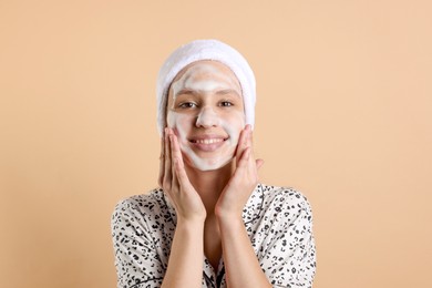 Photo of Teenage girl washing her face with cleanser on beige background. Cosmetic product