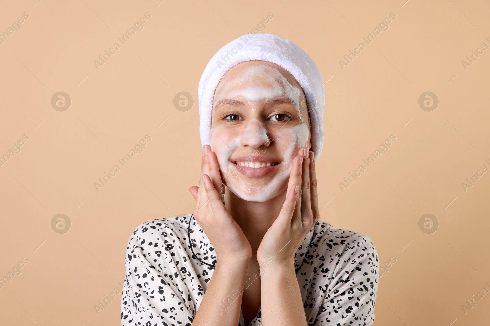 Photo of Teenage girl washing her face with cleanser on beige background. Cosmetic product