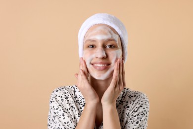 Photo of Teenage girl washing her face with cleanser on beige background. Cosmetic product