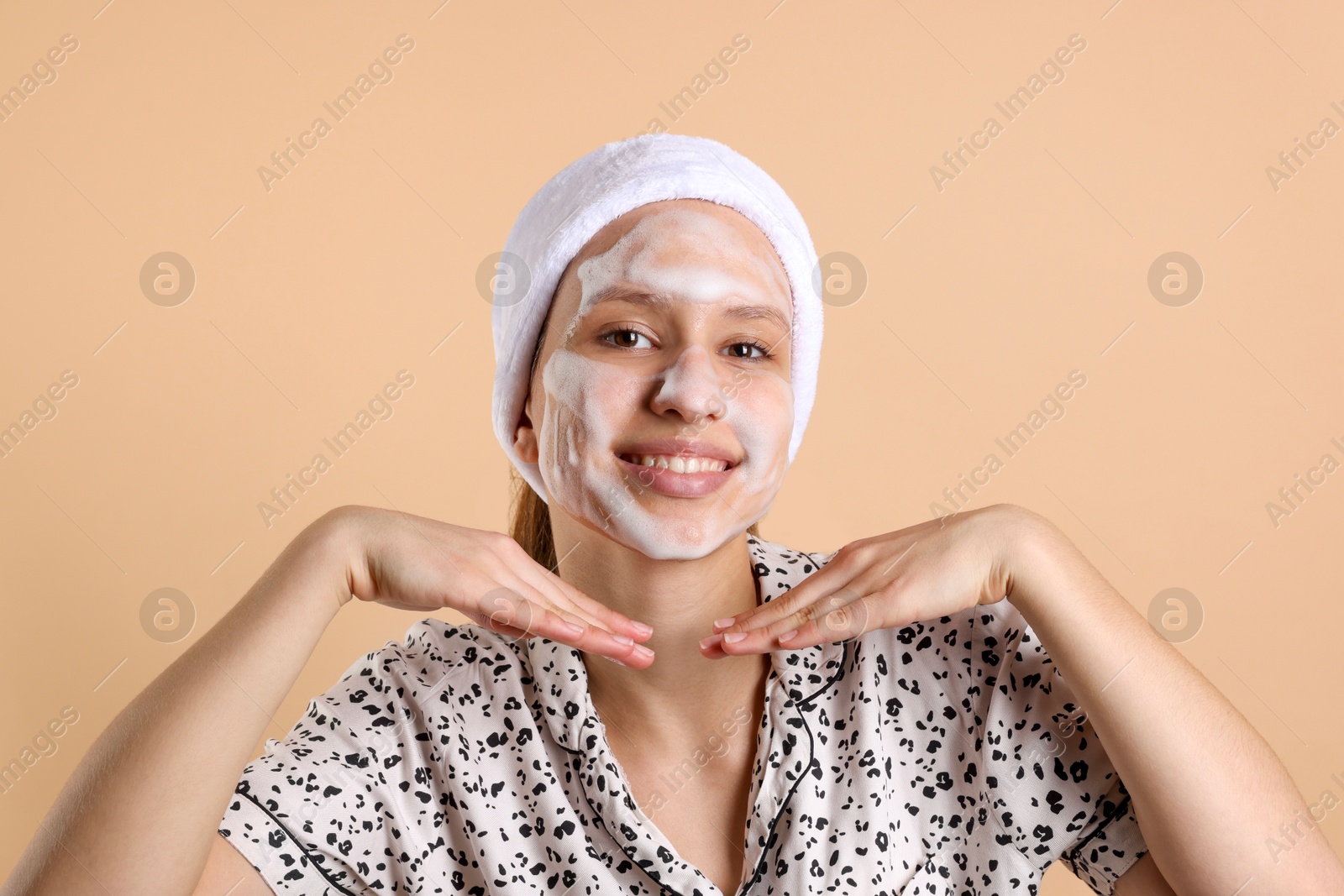 Photo of Teenage girl washing her face with cleanser on beige background. Cosmetic product