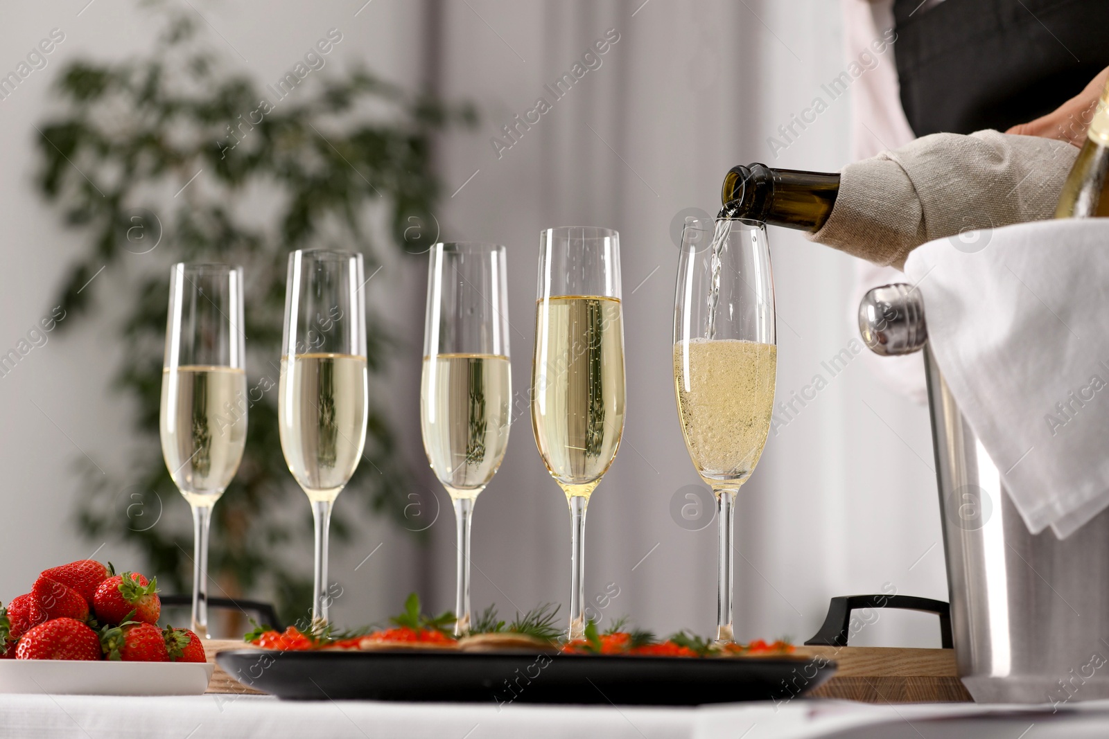 Photo of Waiter filling glasses with champagne indoors, closeup