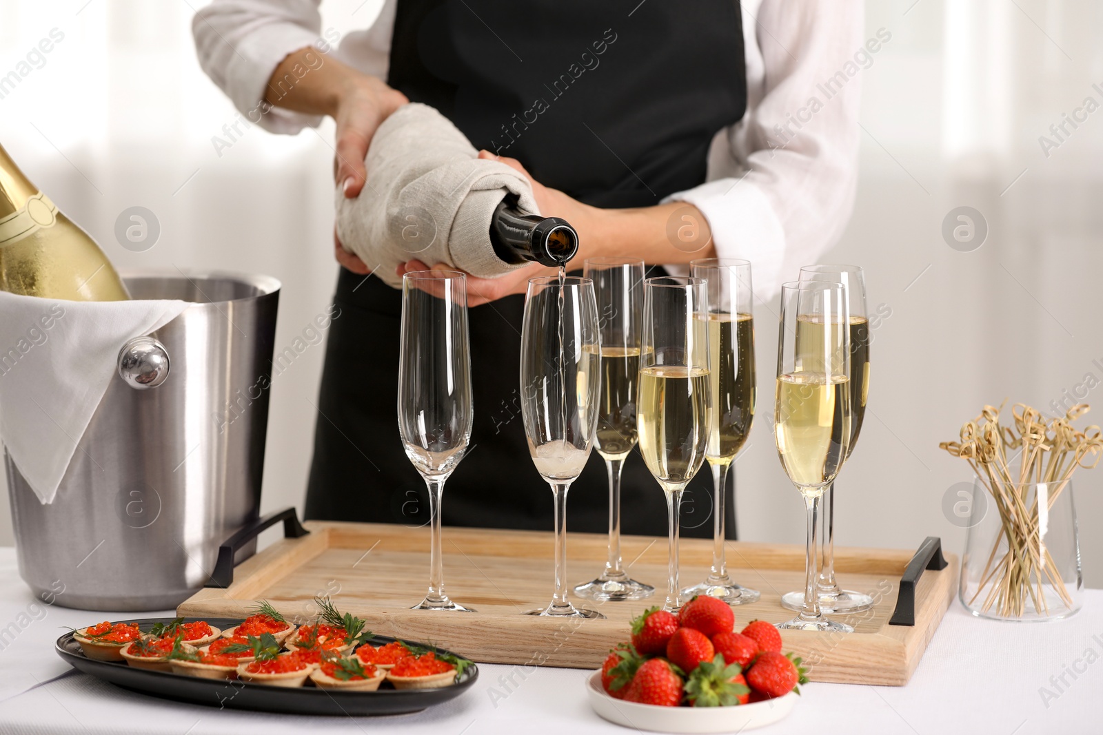 Photo of Waiter filling glasses with champagne indoors, closeup