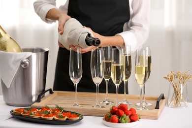 Photo of Waiter filling glasses with champagne indoors, closeup