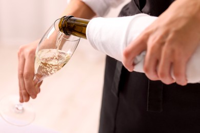 Photo of Waiter pouring champagne into glass indoors, closeup