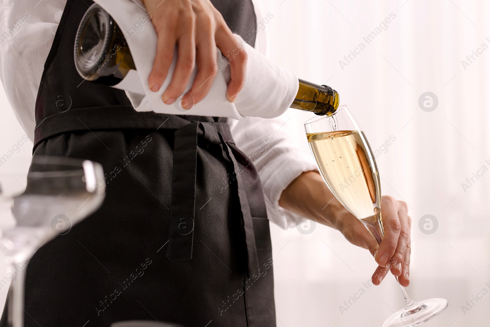 Photo of Waiter pouring champagne into glass indoors, closeup