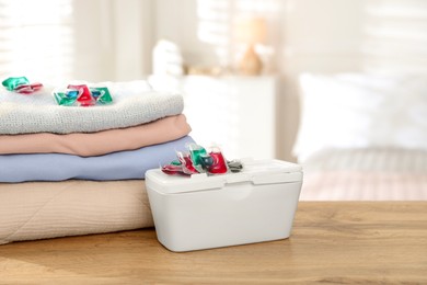 Photo of Detergent capsules in container and clean laundry on wooden table indoors. Space for text