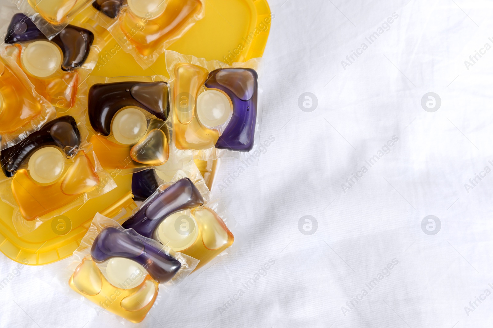 Photo of Laundry detergent capsules in container on white fabric, closeup. Space for text