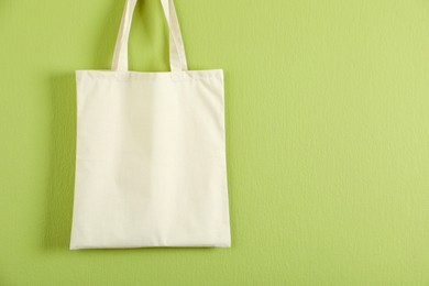 Photo of One eco bag hanging on green wall. Mockup for design