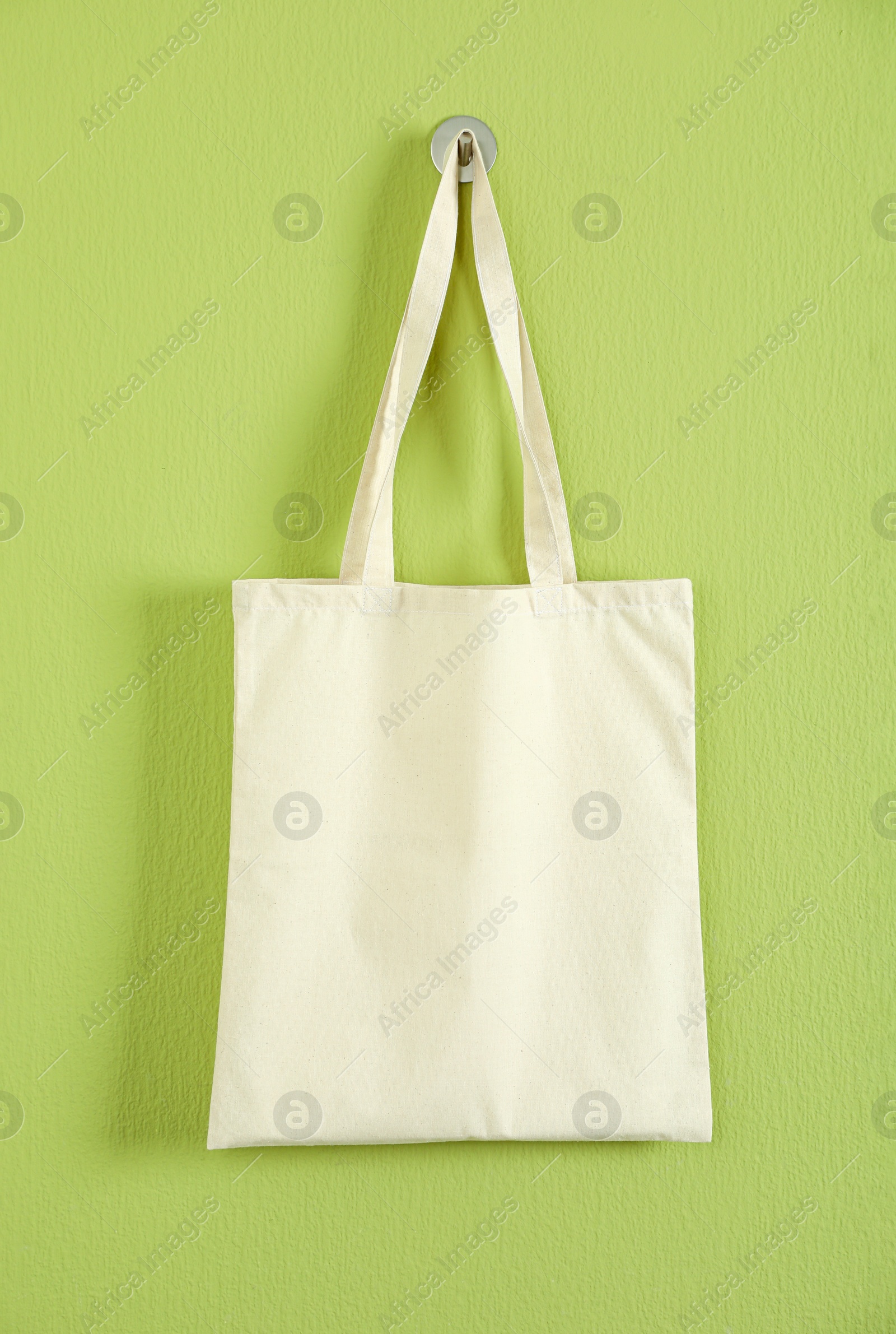 Photo of One eco bag hanging on green wall. Mockup for design