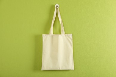 Photo of One eco bag hanging on green wall. Mockup for design