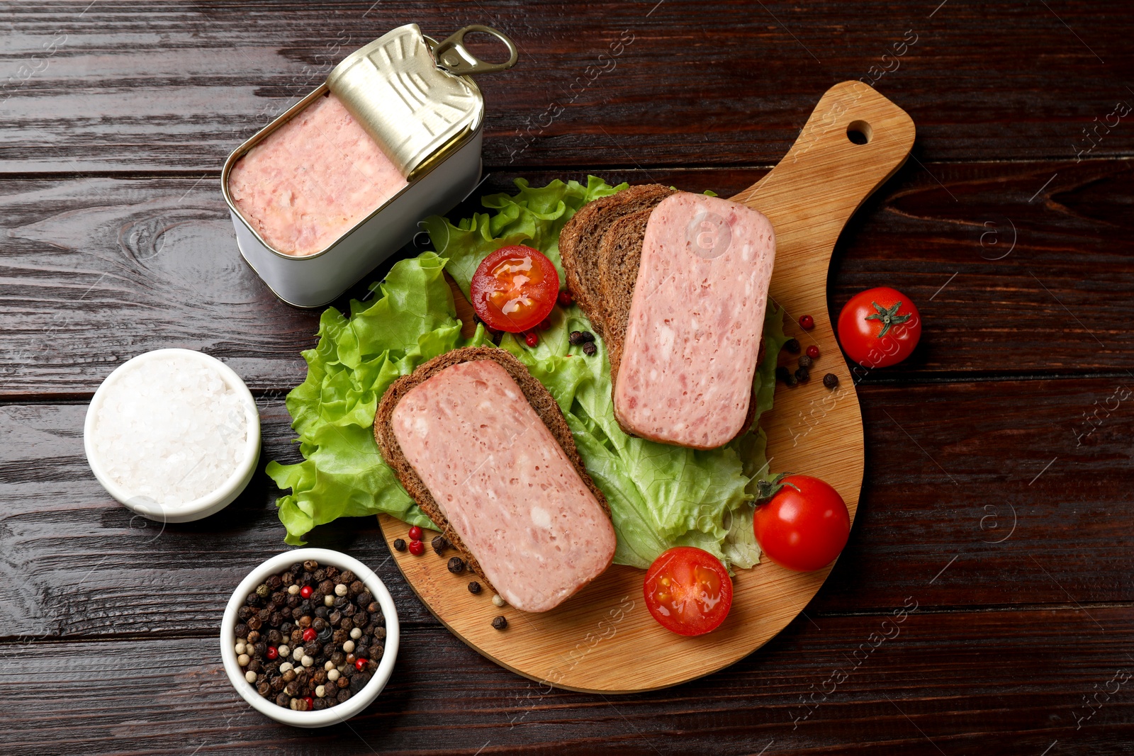 Photo of Tasty canned meat, bread, tomatoes, spices and lettuce on wooden table, top view