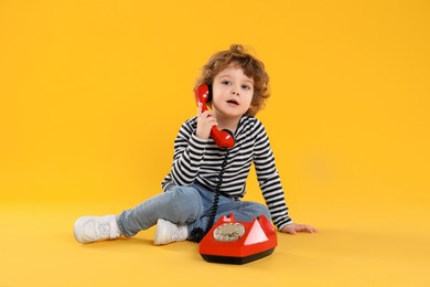 Photo of Cute little boy with telephone on orange background