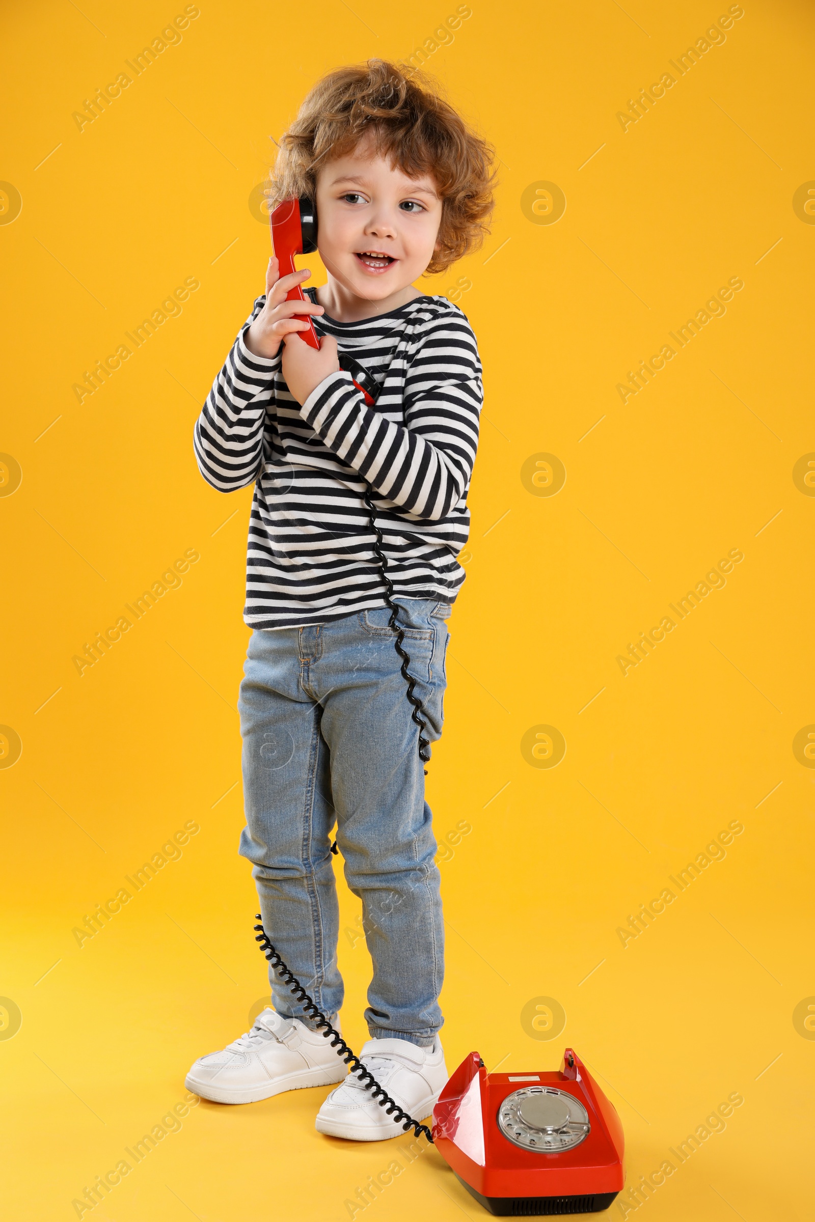 Photo of Cute little boy with telephone on orange background