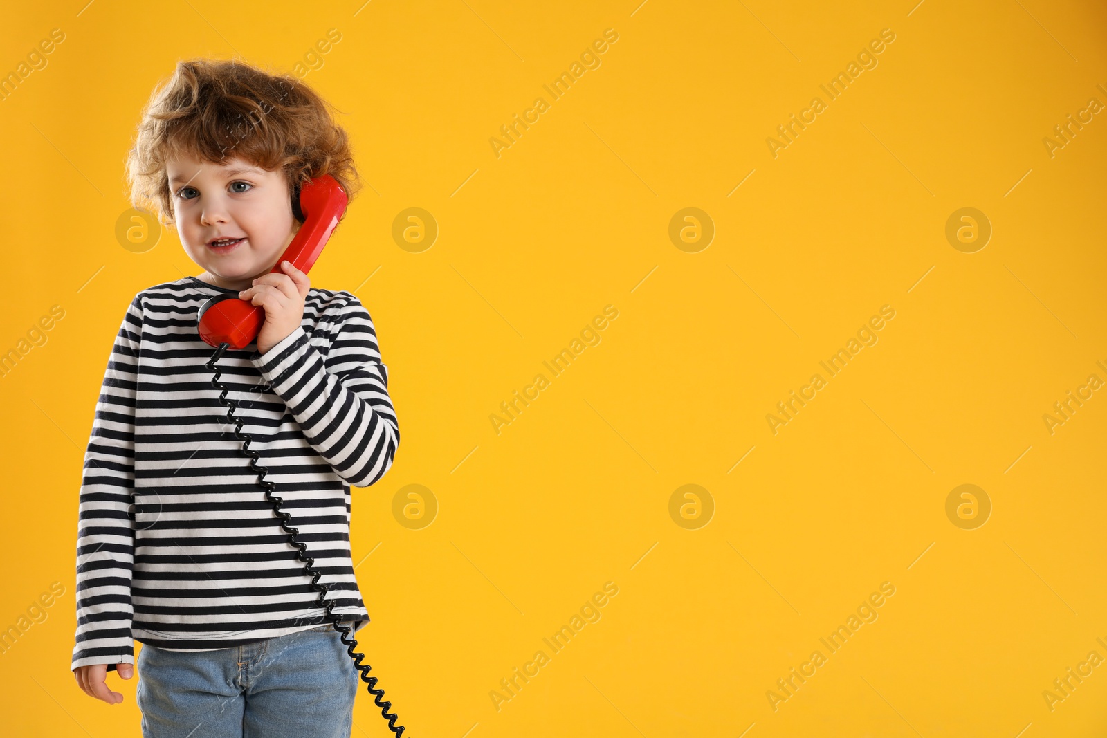 Photo of Cute little boy with telephone handset on orange background, space for text