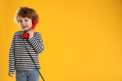 Photo of Cute little boy with telephone handset on orange background, space for text