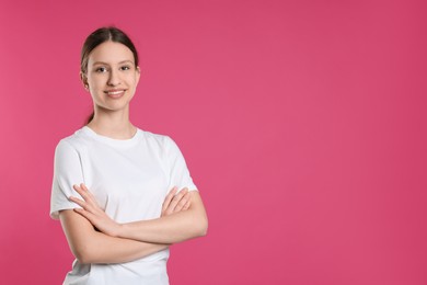 Photo of Portrait of smiling teenage girl with crossed arms on pink background. Space for text