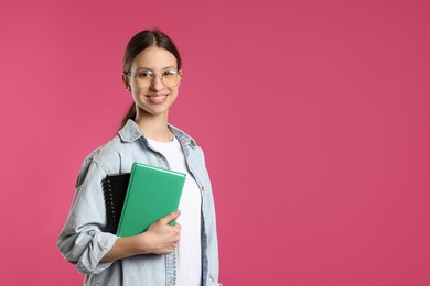 Photo of Portrait of smiling teenage girl with books on pink background. Space for text