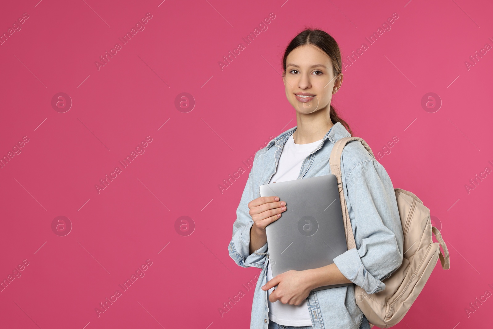 Photo of Portrait of smiling teenage girl with laptop on pink background. Space for text