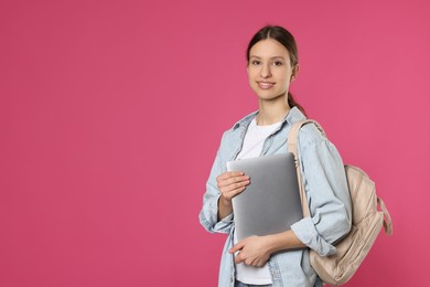 Photo of Portrait of smiling teenage girl with laptop on pink background. Space for text