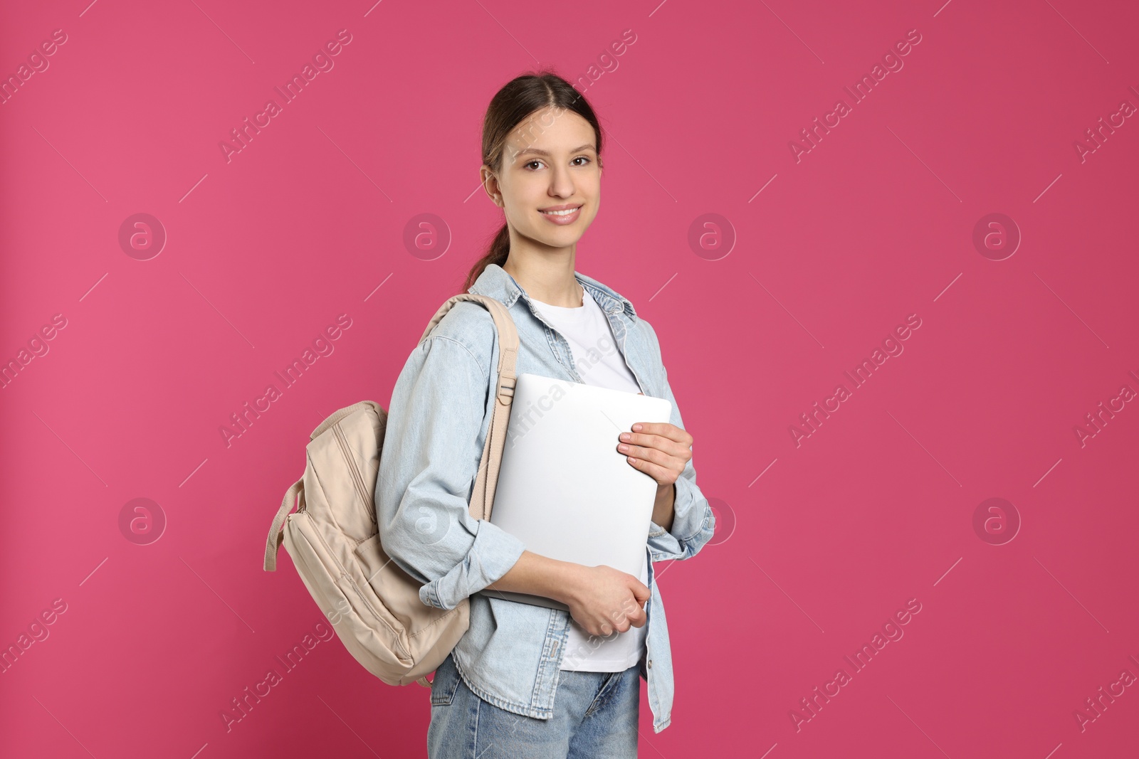 Photo of Portrait of smiling teenage girl with laptop on pink background