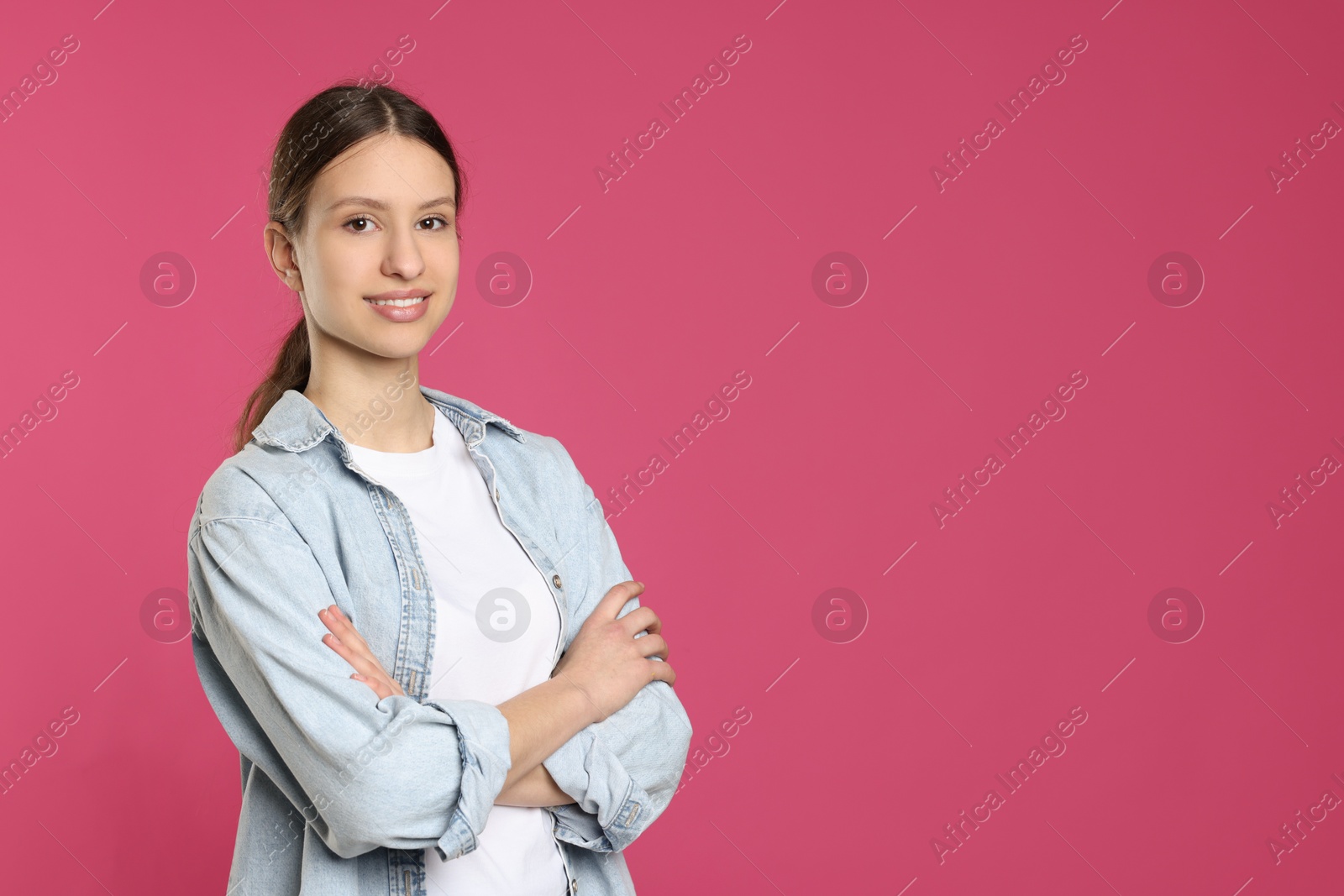 Photo of Portrait of smiling teenage girl with crossed arms on pink background. Space for text