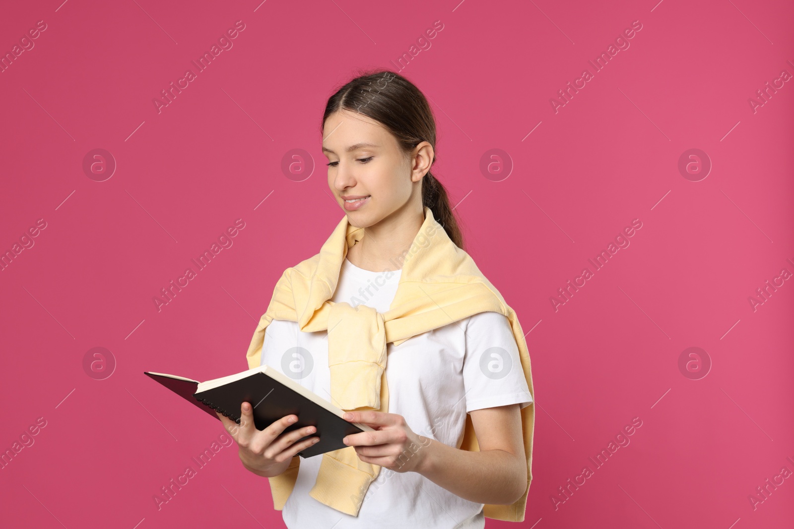 Photo of Portrait of smiling teenage girl reading book on pink background