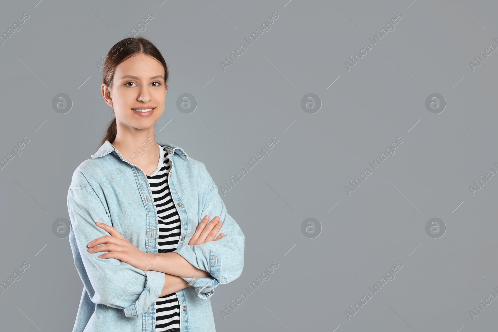 Photo of Portrait of smiling teenage girl with crossed arms on grey background. Space for text