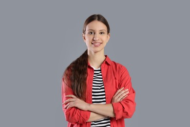 Photo of Portrait of smiling teenage girl with crossed arms on grey background