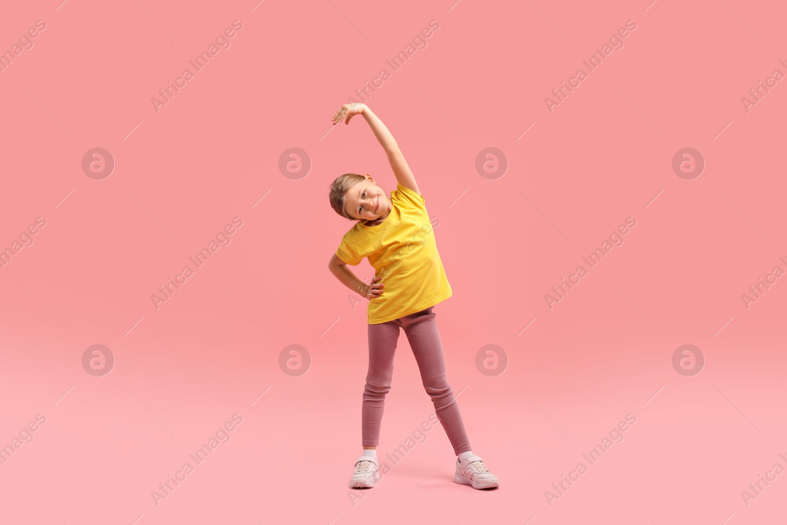 Photo of Cute little girl exercising on pink background