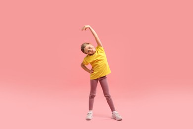 Photo of Cute little girl exercising on pink background