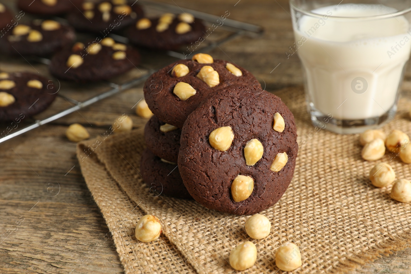 Photo of Tasty chocolate cookies with hazelnuts and milk on wooden table, closeup